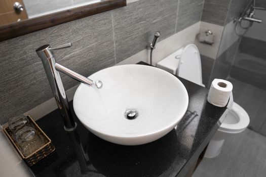 Bathroom interior with white round sink and chrome faucet in a modern bathroom. Water flowing from the chrome faucet