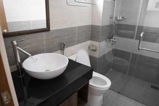 Bathroom interior with white round sink and chrome faucet in a modern bathroom with a toilet and shower. Water flowing from the chrome faucet