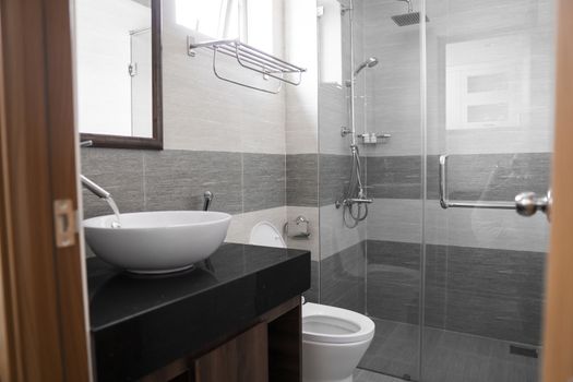 Bathroom interior with white round sink and chrome faucet in a modern bathroom with a toilet and shower. Water flowing from the chrome faucet