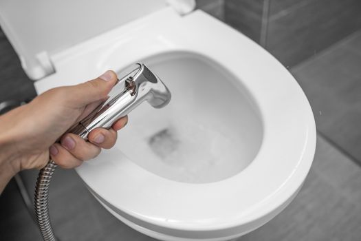 Using of bidet shower with a white toilet. Bidet shower in male hand for using with a white toilet bowl