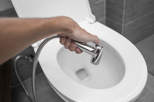 Using of bidet shower with a white toilet. Bidet shower in male hand for using with a white toilet bowl