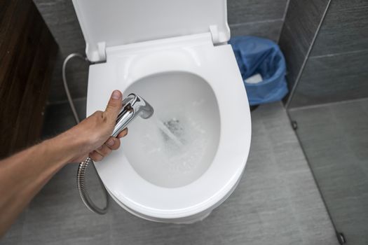 Using of bidet shower with a white toilet. Bidet shower in male hand for using with a white toilet bowl