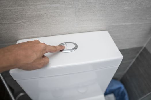 Close up of finger pushing a flush toilet button for cleaning a toilet