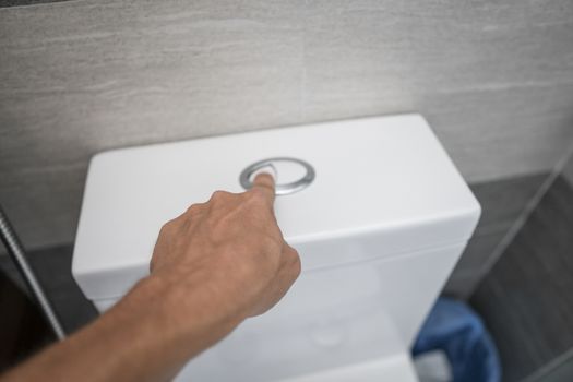 Close up of finger pushing a flush toilet button for cleaning a toilet