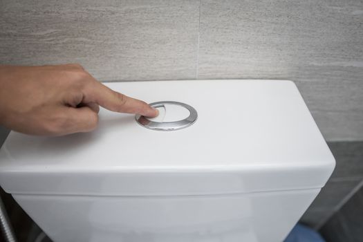 Close up of finger pushing a flush toilet button for cleaning a toilet
