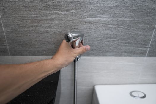 Using of bidet shower in bathroom with a bidet or toiler. Bidet shower in male hand for using it in a bathroom