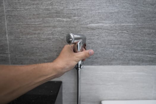 Using of bidet shower in bathroom with a bidet or toiler. Bidet shower in male hand for using it in a bathroom