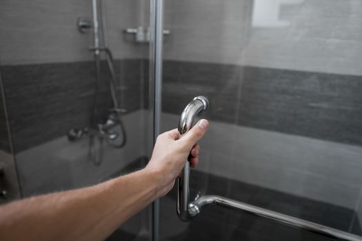 Male hand opens the shower door in a modern bathroom