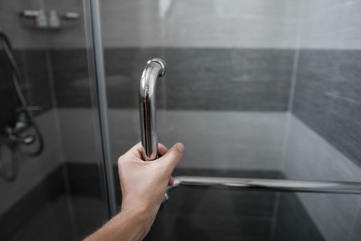 Male hand opens the shower door in a modern bathroom