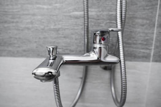 Modern designer tap and shower in bathroom. Closeup of chrome shower, faucet, in the bathroom covered decorative ceramic. Mixer cold hot water