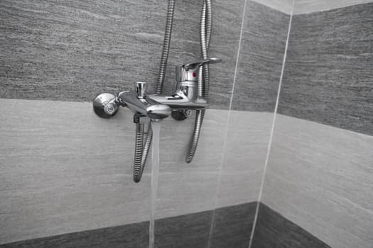Water flows from the mixer. Modern designer tap and shower in bathroom. Closeup of chrome shower, faucet, in the bathroom covered decorative ceramic. Mixer cold hot water