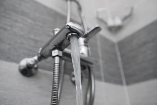 Water flows from the mixer. Modern designer tap and shower in bathroom. Closeup of chrome shower, faucet, in the bathroom covered decorative ceramic. Mixer cold hot water