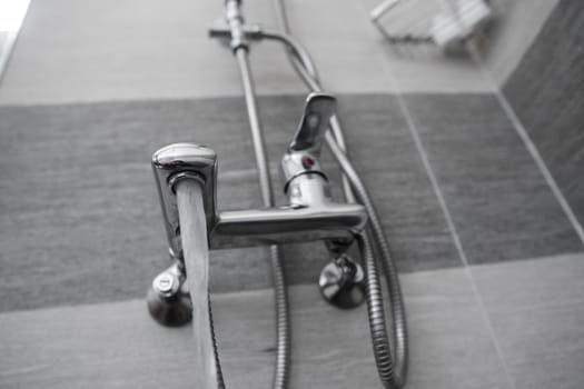 Water flows from the mixer. Modern designer tap and shower in bathroom. Closeup of chrome shower, faucet, in the bathroom covered decorative ceramic. Mixer cold hot water