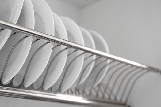 Dish drying metal rack with big nice white clean plates. Traditional comfortable kitchen. Open white dish draining closet with wet dishes of glass and ceramic, plates, bowls drying inside on rack