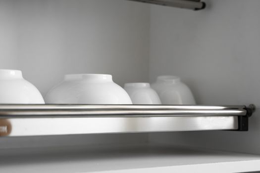 Dish drying metal rack with big nice white clean plates. Traditional comfortable kitchen. Open white dish draining closet with wet dishes of glass and ceramic, plates, bowls drying inside on rack