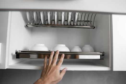 Dish drying metal rack with big nice white clean plates. Traditional comfortable kitchen. Open white dish draining closet with wet dishes of glass and ceramic, plates, bowls drying inside on rack