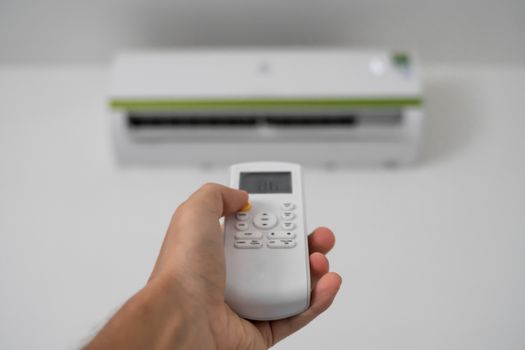 Man's hand using remote controler. Hand holding rc and adjusting temperature of air conditioner mounted on a white wall. Indooor comfort temperature. Health concepts and energy savings