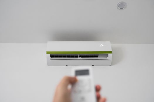 Man's hand using remote controler. Hand holding rc and adjusting temperature of air conditioner mounted on a white wall. Indooor comfort temperature. Health concepts and energy savings