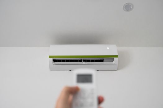 Man's hand using remote controler. Hand holding rc and adjusting temperature of air conditioner mounted on a white wall. Indooor comfort temperature. Health concepts and energy savings