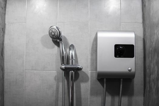 Instant tankless electric water heater installed on grey tile wall with input and output pipe outlet and elcb safety breaker system and silver shower