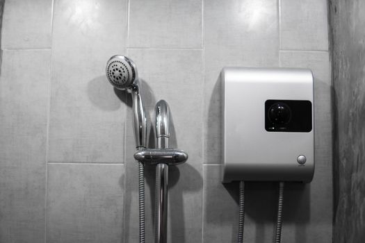 Instant tankless electric water heater installed on grey tile wall with input and output pipe outlet and elcb safety breaker system and silver shower