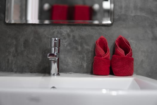 Modern stainless steel faucet with wash basin sink with a two red towels on it . Counter bathroom interior contemporary. Luxury and stylish design bathroom with a concrete style walls