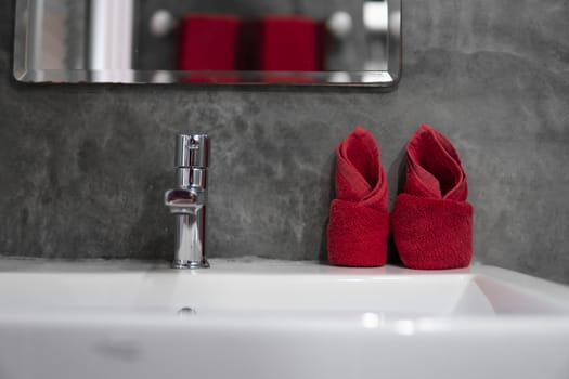 Modern stainless steel faucet with wash basin sink with a two red towels on it . Counter bathroom interior contemporary. Luxury and stylish design bathroom with a concrete style walls