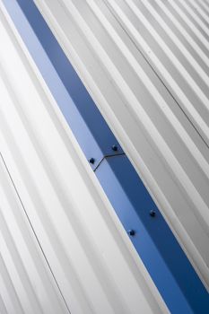 Metal corrugated sheets on a building with a blue metal corners. White aluminium metal corrugated roof or wall sheets on a factories and industrial buildings