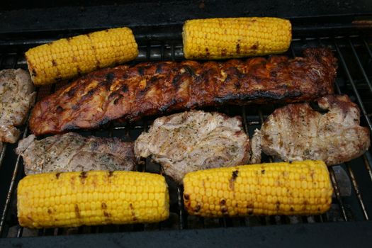 Several pieces of grilled meat and corn on the cob on a grill