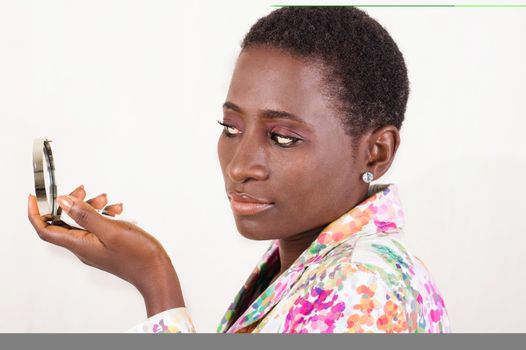 Young African woman looks at the small mirror to see the beauty of her makeup.