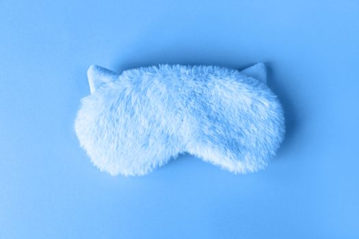 Fluffy fur sleep mask with small ears on paper background. Top view, flatlay. Accessories for girls and young women in Classic Blue colour, close-up, top view. Color of the year 2020 concept.