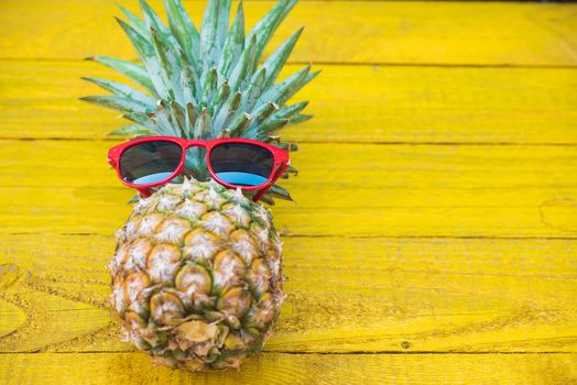 Holiday pineapple have sunglasses on yellow  wooden background, tropical holiday concept