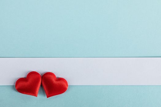 Valentine's day two red silk hearts and white paper on blue paper background, love concept