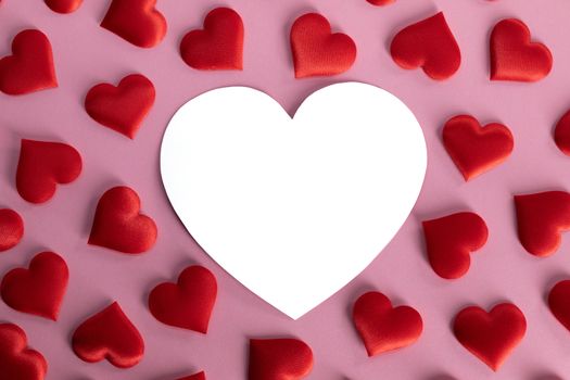 Valentine's day many red silk hearts and white heart shaped card on pink background, love concept