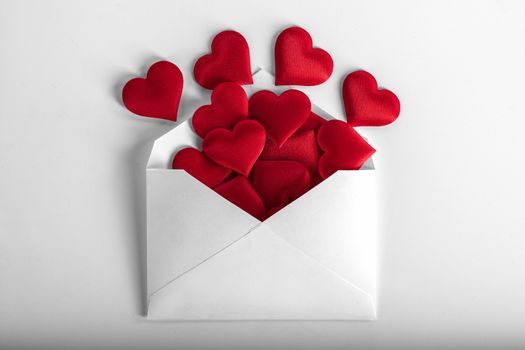 Valentine day love letter, envelope of white paper with red hearts heap spread on white background.