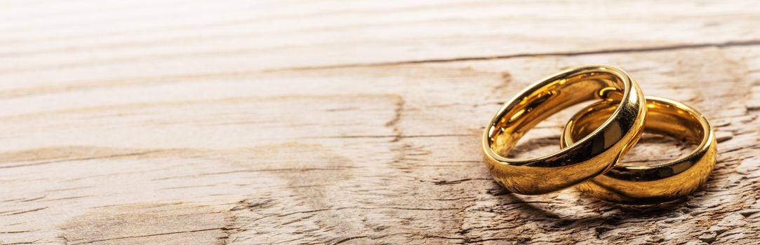 Two golden wedding rings on wooden background with copy space for text