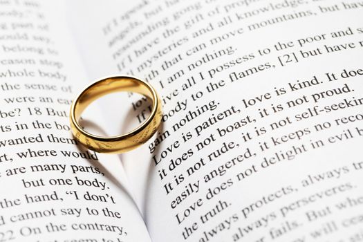 One golden wedding ring on Holy bible book with heart shaped shadow close up