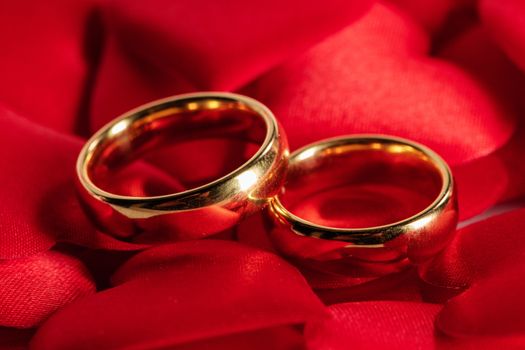 Two golden wedding rings on red satin hearts background