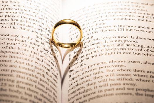 One golden wedding ring on Holy bible book with heart shaped shadow close up