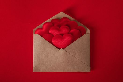 Valentine day love letter, envelope of craft paper with red hearts heap spread on red background.