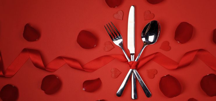 Cutlery set tied with silk ribbon rose petals and hearts on red background Valentine day romantic dinner concept