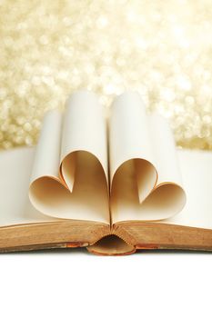 Blank pages of open book rolled in heart shape on glitter background
