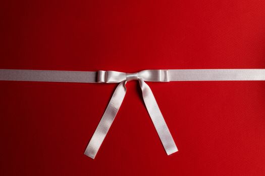 White satin ribbon bow on red paper background
