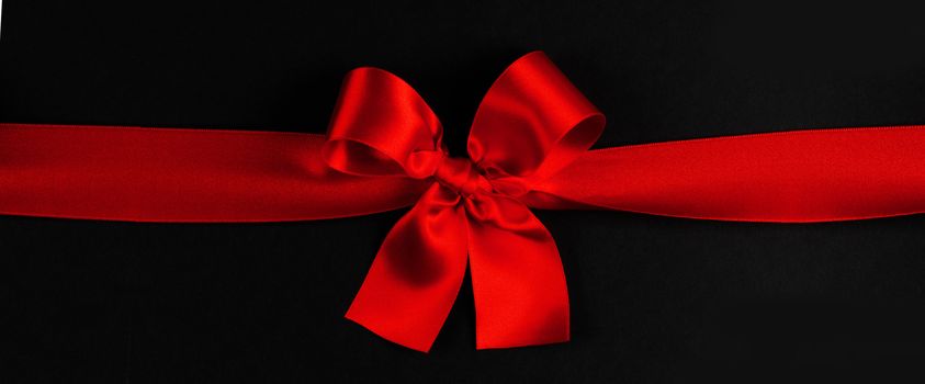 Red satin ribbon bow on black paper background