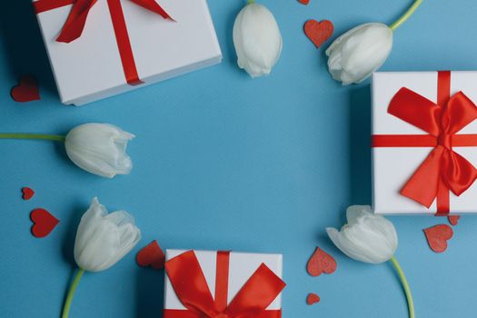 White tulip flowers gifts red hearts and gifts composition on blue background top view with copy space. Valentine's day, birthday, wedding, Mother's day concept. Copy space