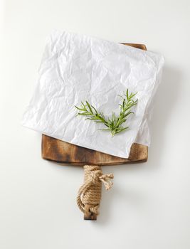 Creased sheet of white wax paper and fresh rosemary on cutting board