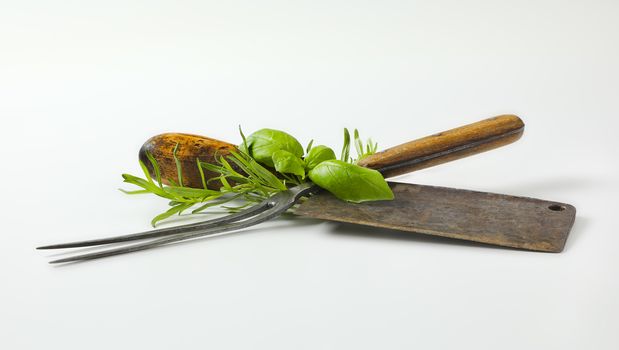 Old meat cleaver knife, carving fork and fresh culinary herbs