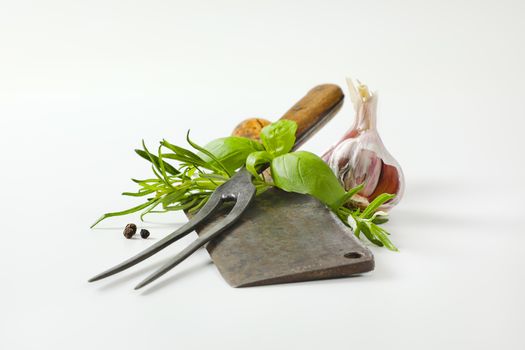 Vintage meat cleaver knife, carving fork, fresh culinary herbs, garlic and peppercorns