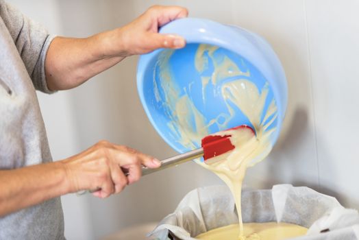 Senior woman hands pouring dough into a baking tray. Shallow deep of field.