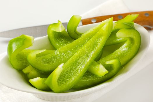 Sliced green bell pepper in white bowl and kitchen knife next to it
